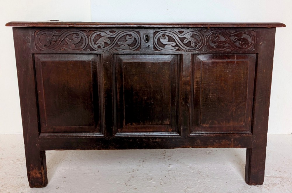 A dark oak 17th-century coffer featuring three front panels and a carved scrollwork frieze below the hinged lid. View VII