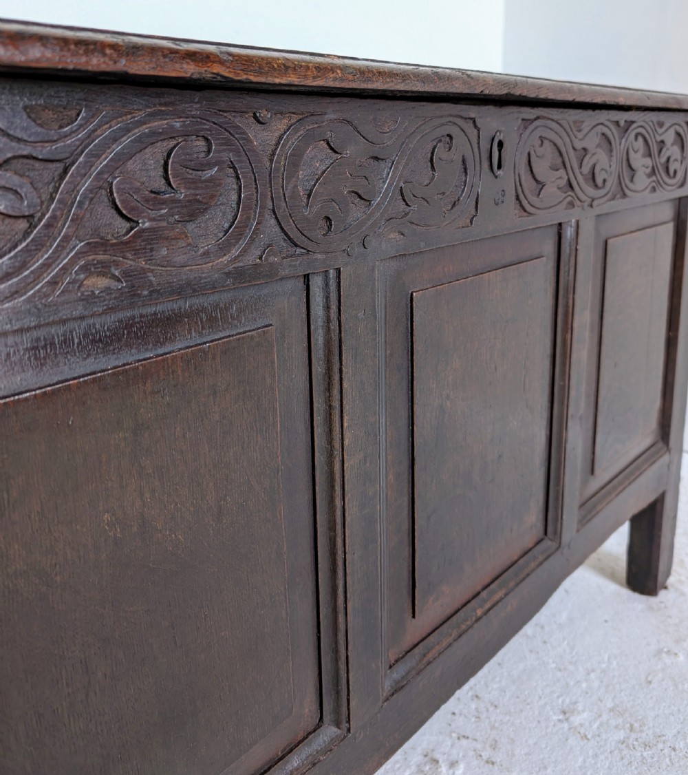 A dark oak 17th-century coffer featuring three front panels and a carved scrollwork frieze below the hinged lid. View VIII