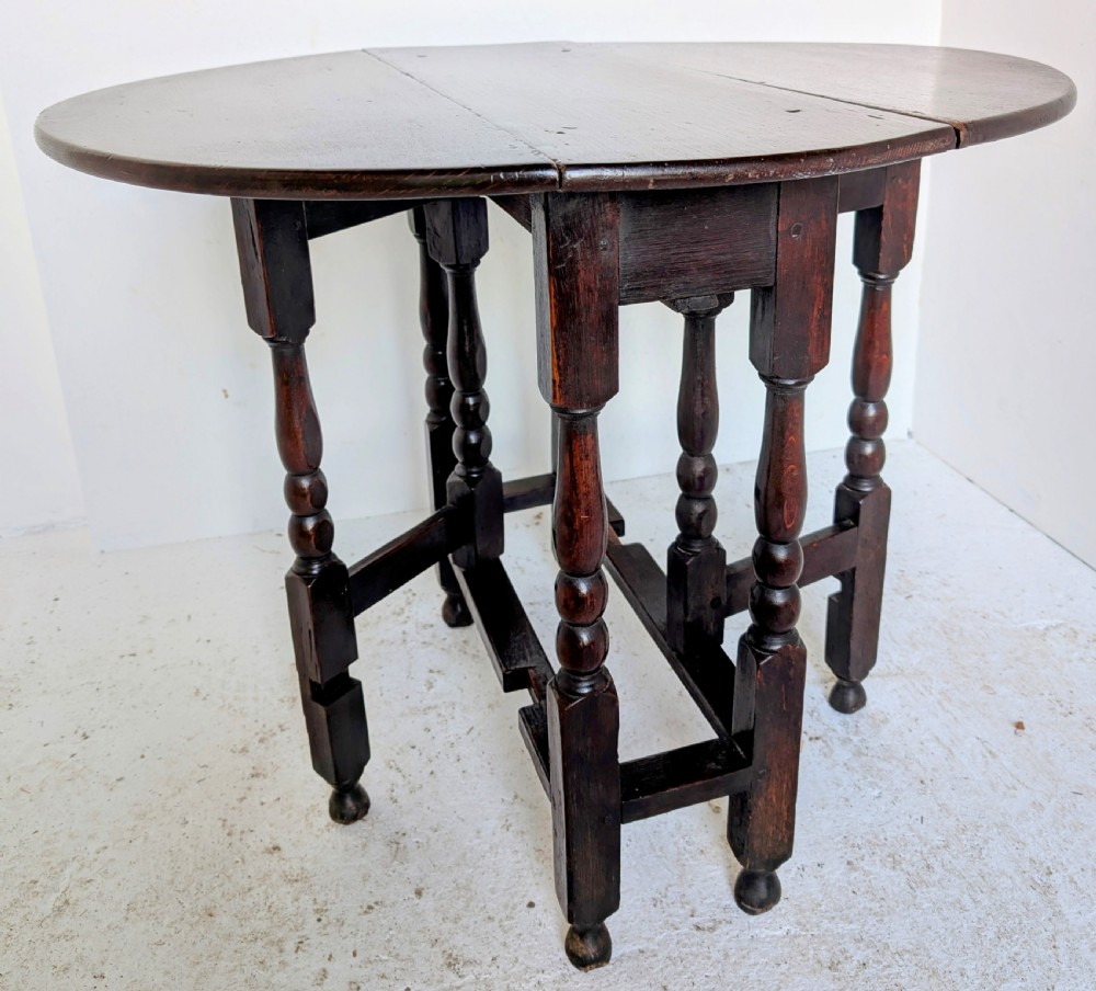 A dark oak 17th-century gateleg table with two drop-leaf flaps, turned baluster legs, and low box stretchers.