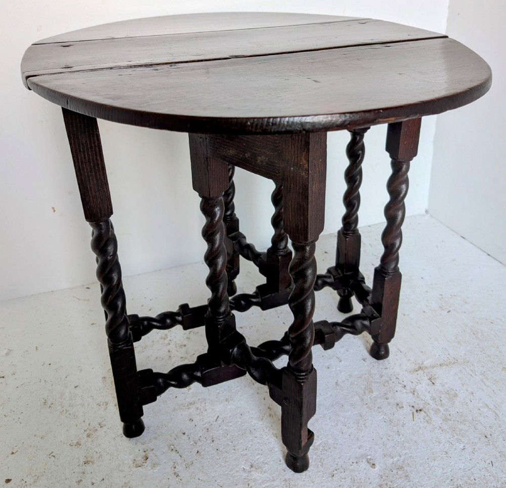 A small dark oak gateleg table featuring a drop-leaf top, barley twist legs, and lower connecting stretchers.