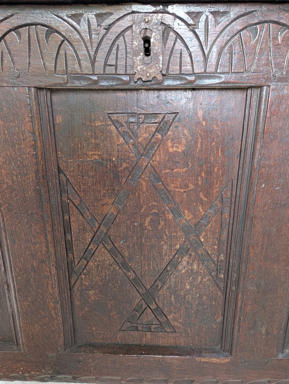 A 17th-century dark carved oak coffer featuring a three-panel hinged top and carved geometric patterns on the front panels. View II