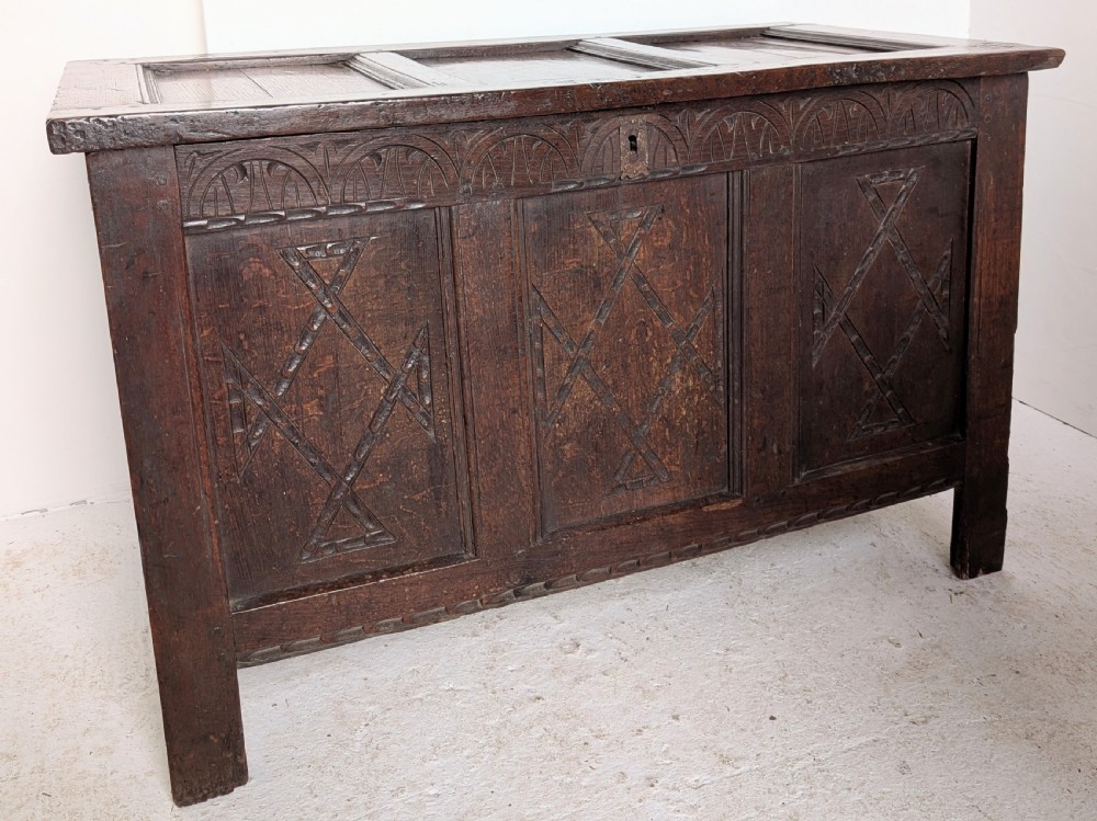 A 17th-century dark carved oak coffer featuring a three-panel hinged top and carved geometric patterns on the front panels. View IV