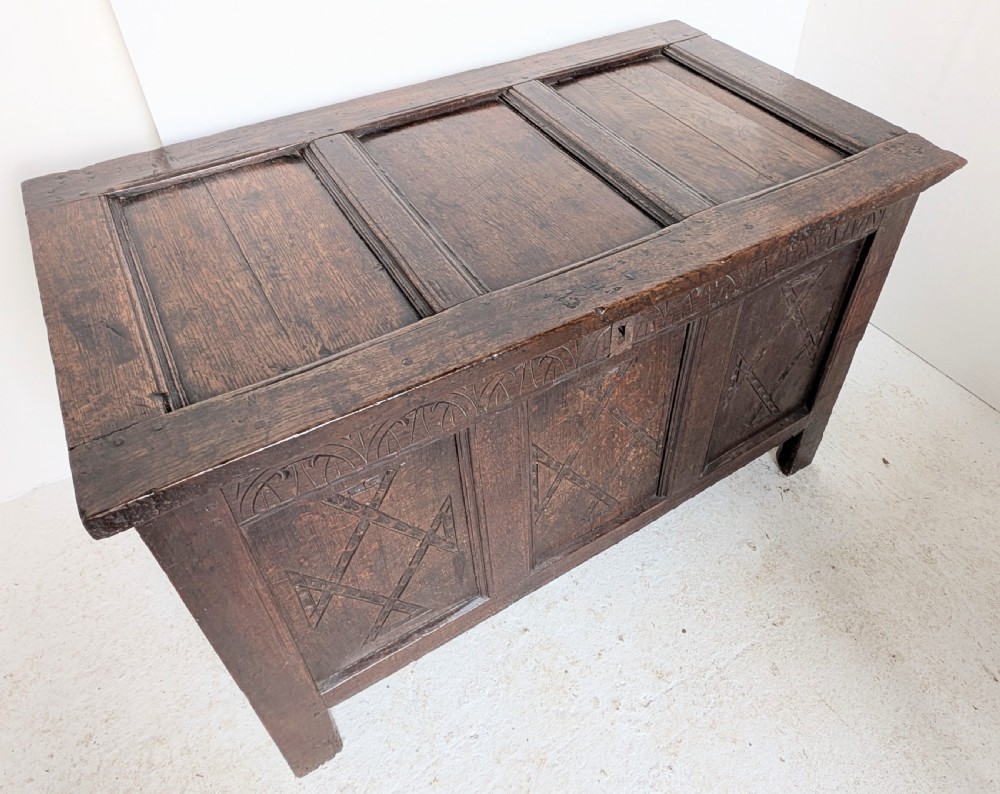 A 17th-century dark carved oak coffer featuring a three-panel hinged top and carved geometric patterns on the front panels. View V