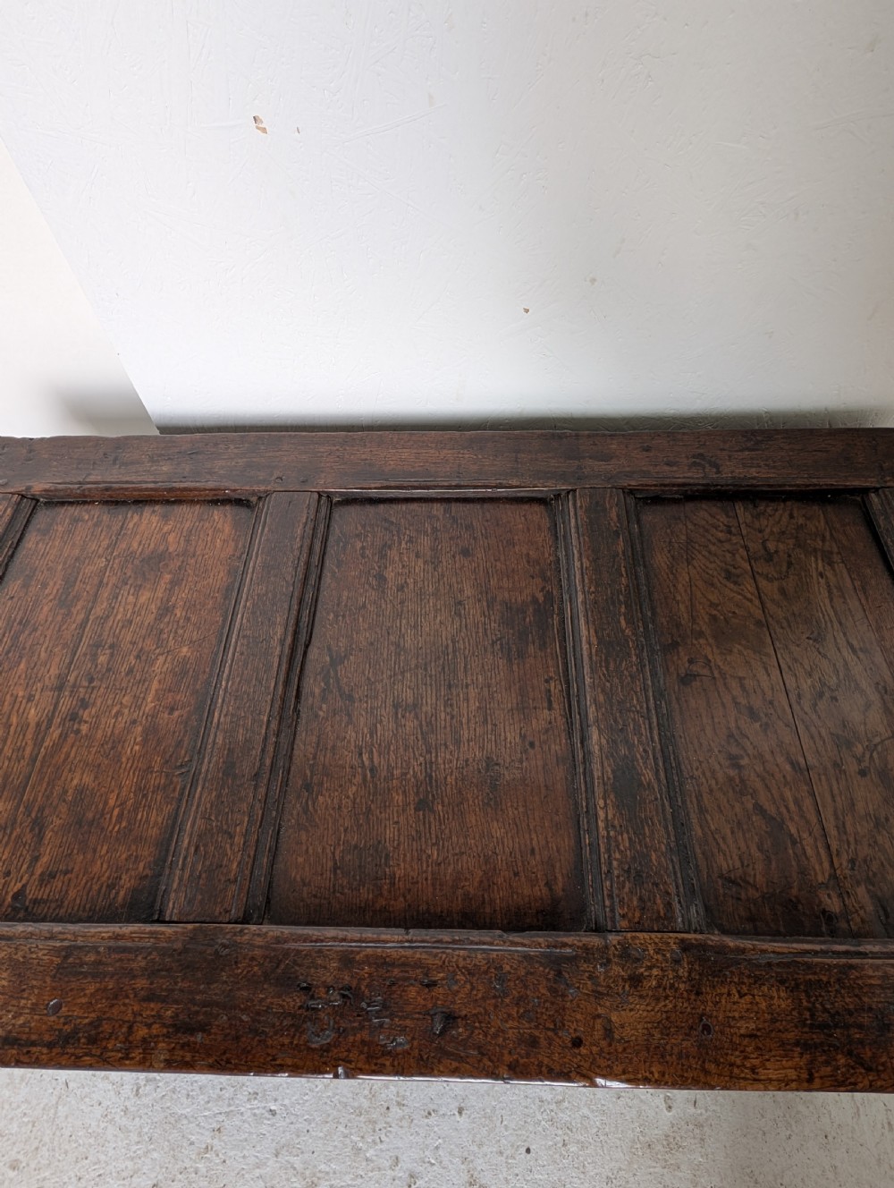 A 17th-century dark carved oak coffer featuring a three-panel hinged top and carved geometric patterns on the front panels. View VI