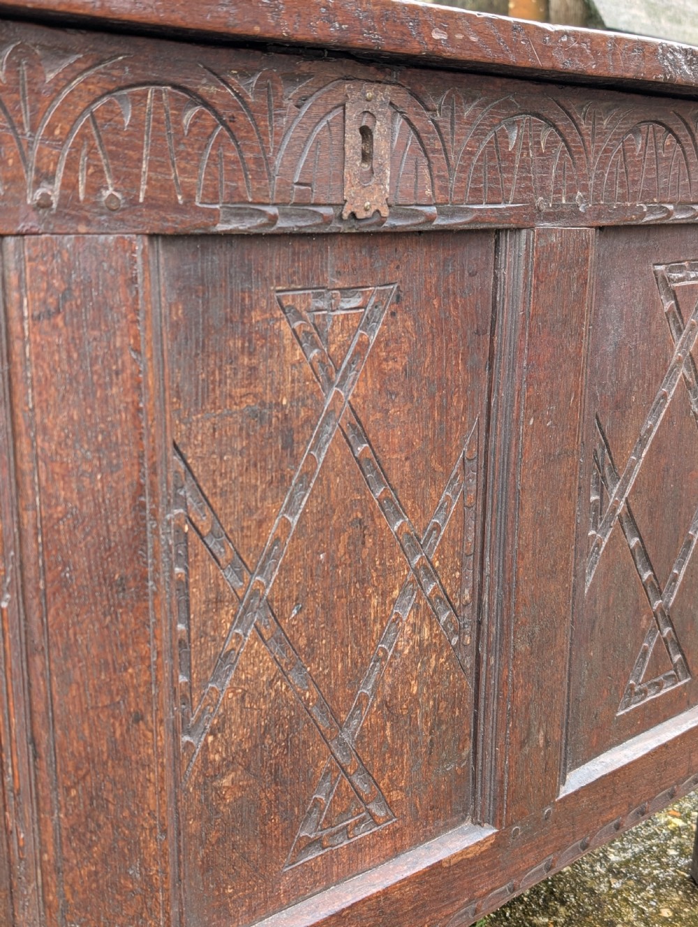 A 17th-century dark carved oak coffer featuring a three-panel hinged top and carved geometric patterns on the front panels. View VII