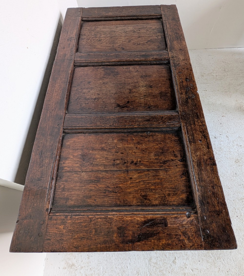 A 17th-century dark carved oak coffer featuring a three-panel hinged top and carved geometric patterns on the front panels. View VIII