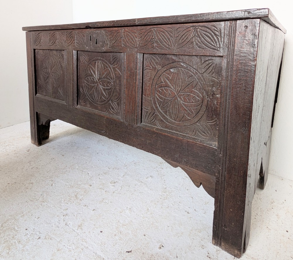A dark brown 17th century oak coffer featuring three carved panel fronts with circular rosette motifs and a hinged lid.
