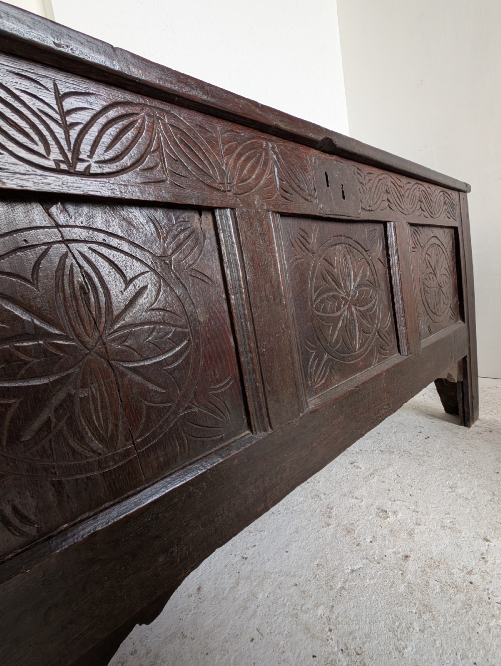 A dark brown 17th century oak coffer featuring three carved panel fronts with circular rosette motifs and a hinged lid. View VI