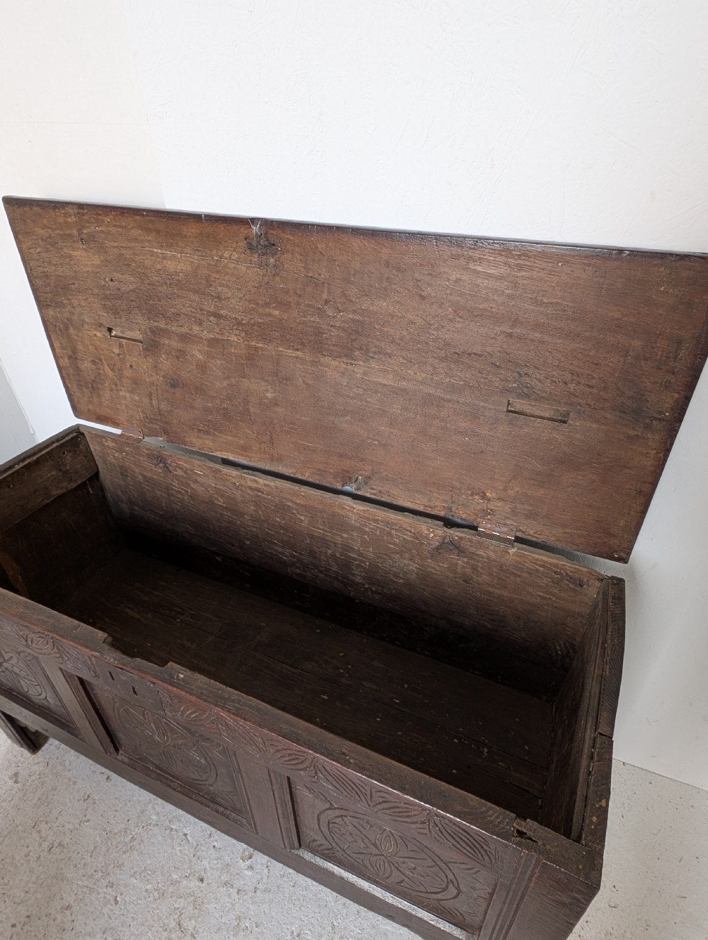 A dark brown 17th century oak coffer featuring three carved panel fronts with circular rosette motifs and a hinged lid. View VII