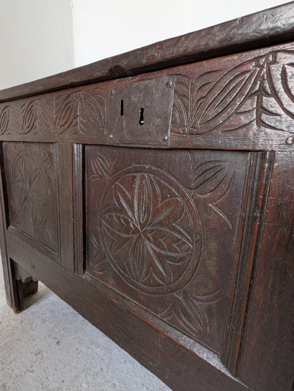 A dark brown 17th century oak coffer featuring three carved panel fronts with circular rosette motifs and a hinged lid. View VIII