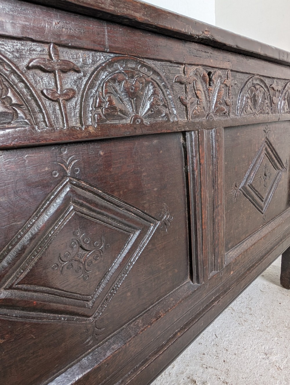 A 17th-century dark oak coffer featuring lunette carving on the upper rail and lozenge panel detailing across the front. View VI