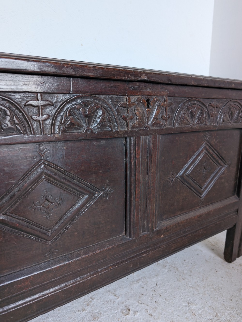 A 17th-century dark oak coffer featuring lunette carving on the upper rail and lozenge panel detailing across the front. View X
