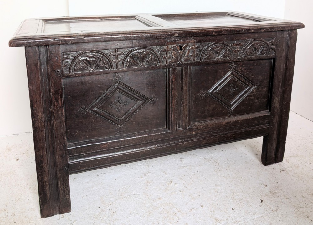 A 17th-century dark oak coffer featuring lunette carving on the upper rail and lozenge panel detailing across the front.