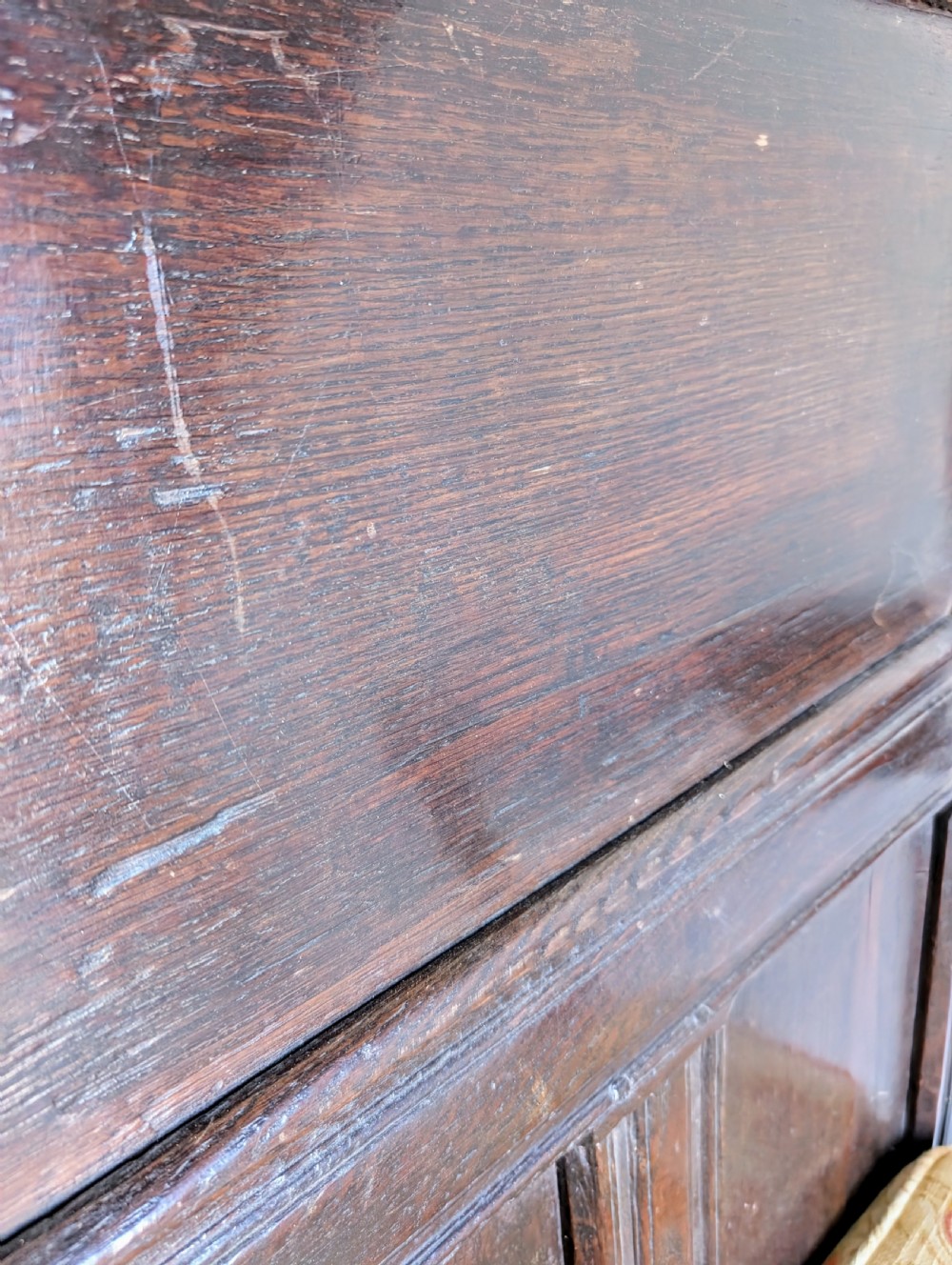 A dark oak 17th-century wainscot armchair featuring a panelled backrest, turned front legs, robust armrests, and an upholstered seat cushion. View III