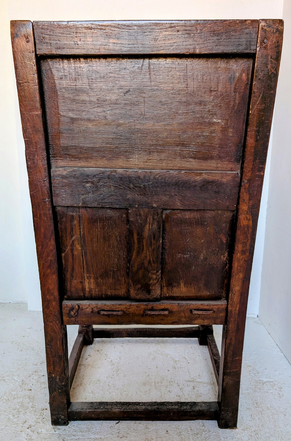 A dark oak 17th-century wainscot armchair featuring a panelled backrest, turned front legs, robust armrests, and an upholstered seat cushion. View VI