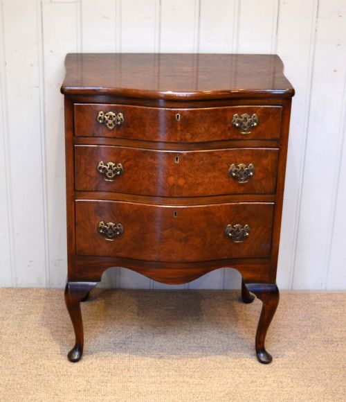 fig 1. A Queen Anne style burr walnut chest of drawers featuring three serpentine drawers with brass handles, supported on tall cabriole legs.