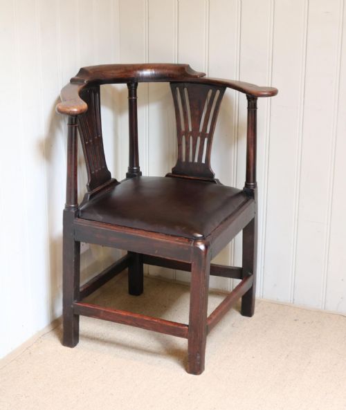 fig 1. An antique dark elm corner chair featuring a curved armrest rail, twin pierced back splats, turned supports, and a dark upholstered seat.