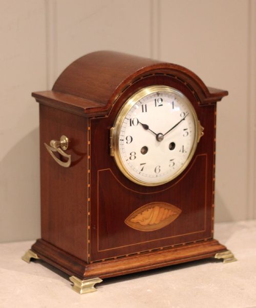 fig 2. A mahogany break-arch mantel clock featuring a shell marquetry inlay, brass bracket feet, side drop handles, and an enamel dial with Arabic numerals.