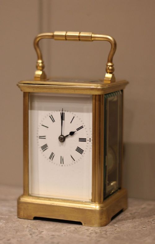 fig 1. An antique French carriage clock featuring a rectangular gilded brass case with a folding handle, clear glass side panels, and a white enamel dial with black Roman numerals.
