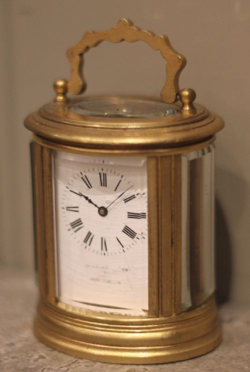 fig 1. A late 19th-century miniature oval brass carriage clock with a white enamel dial alongside its original fitted leather travel case.