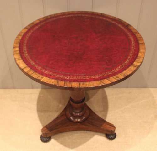fig 1. A Regency circular rosewood occasional table featuring a red leather insert with gold tooling, a turned pedestal stem, and a triform base on lobed feet.