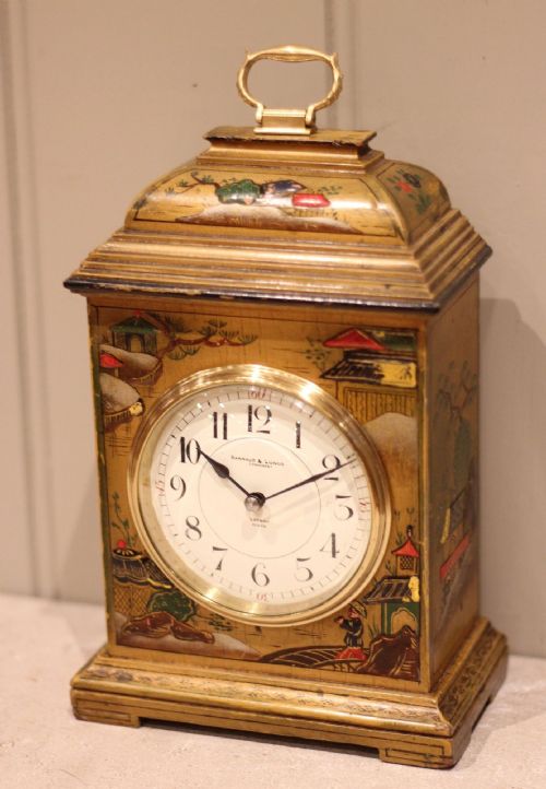fig 1. A small rectangular Chinoiserie lacquered mantel clock decorated with hand-painted gold and polychrome Asian landscapes, featuring a white dial and top brass handle.