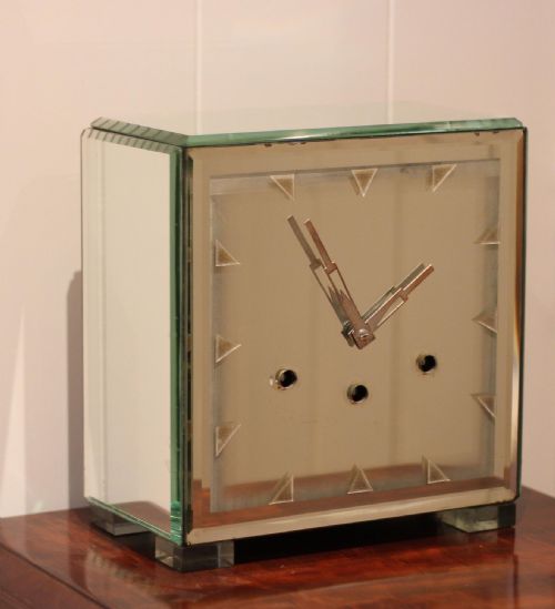 fig 1. A rectangular Art Deco mantel clock clad in bevelled mirrored glass panels with geometric triangular hour markers and three winding key holes on the dial.