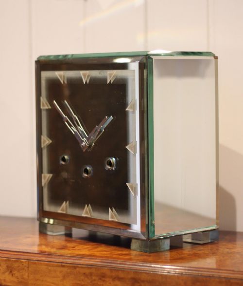 fig 2. A rectangular Art Deco mantel clock clad in bevelled mirrored glass panels with geometric triangular hour markers and three winding key holes on the dial.