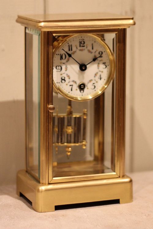 fig 1. A rectangular brass four glass mantel clock featuring bevelled glass panels, a white enamel dial with floral garland decoration, and a visible hanging pendulum.