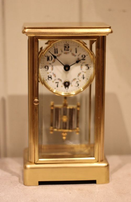fig 2. A rectangular brass four glass mantel clock featuring bevelled glass panels, a white enamel dial with floral garland decoration, and a visible hanging pendulum.
