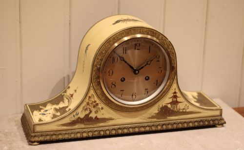 fig 1. An arched cream lacquered mantel clock featuring hand-painted Chinoiserie pagoda landscapes and a brass-rimmed dial with Arabic numerals.