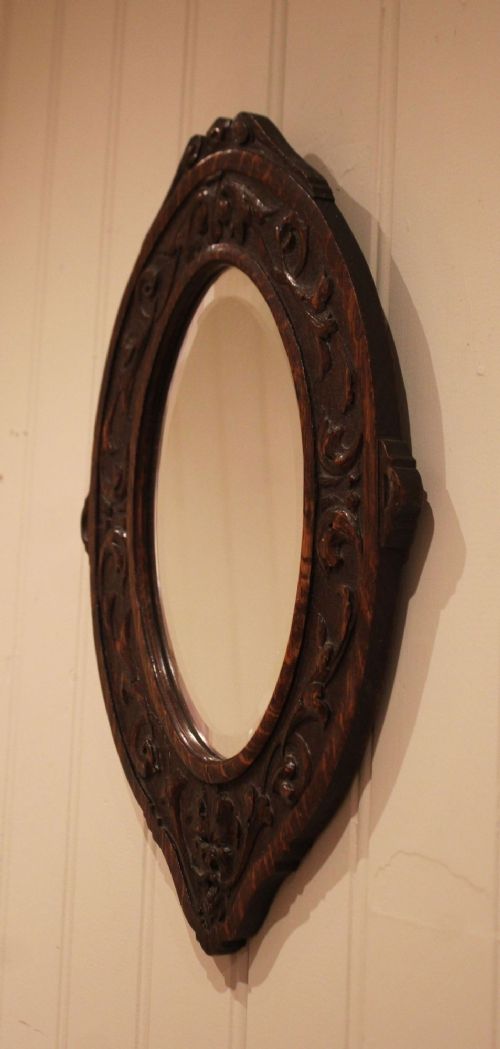 A small oval wall mirror featuring a heavily carved dark oak wooden frame with scroll motifs and a bevelled glass plate. View VIII