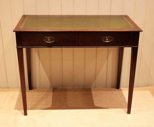 fig 1. An early 19th-century mahogany writing desk featuring a green leather inset top, two frieze drawers with brass oval handles, and square tapered legs.