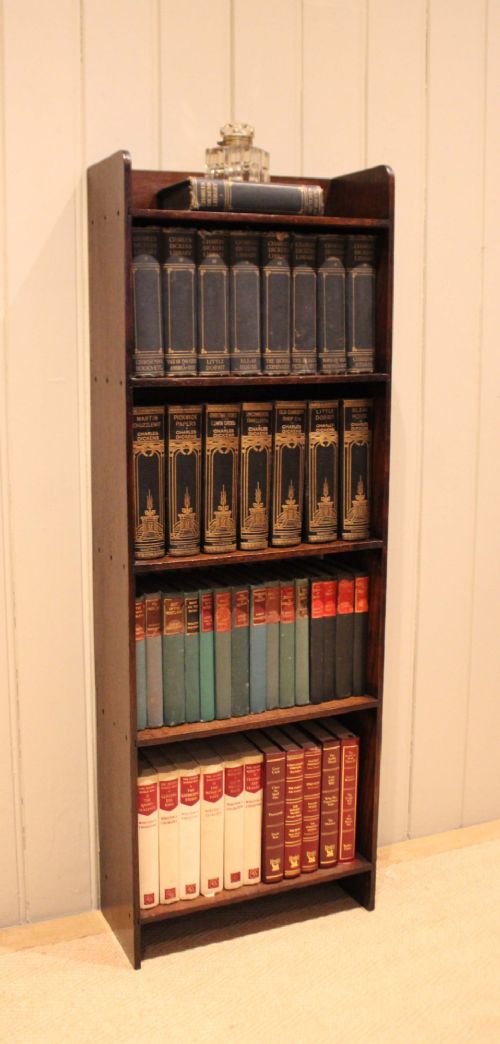 A narrow 1920s dark oak open bookcase featuring four fixed shelves filled with vintage books. View V