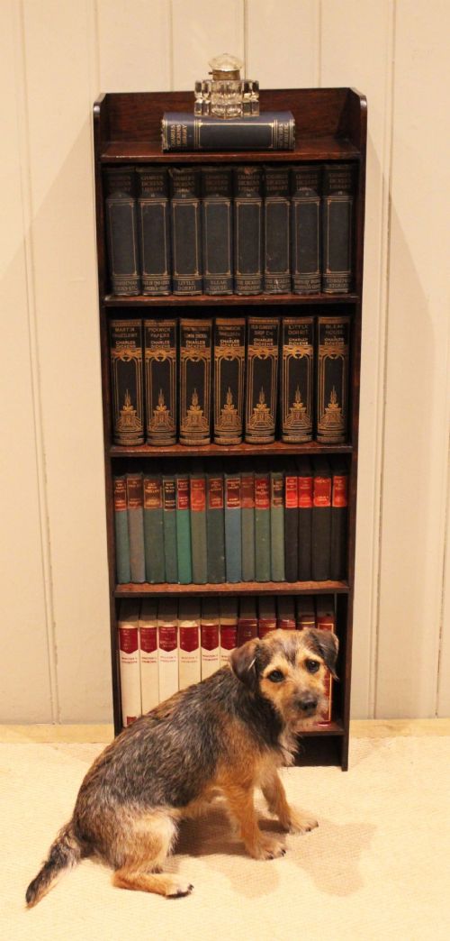 A narrow 1920s dark oak open bookcase featuring four fixed shelves filled with vintage books. View VII