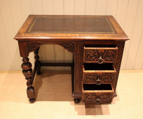 fig 1. A late nineteenth-century dark carved oak writing desk featuring three side drawers with detailed foliate carvings and a leather inset writing surface.