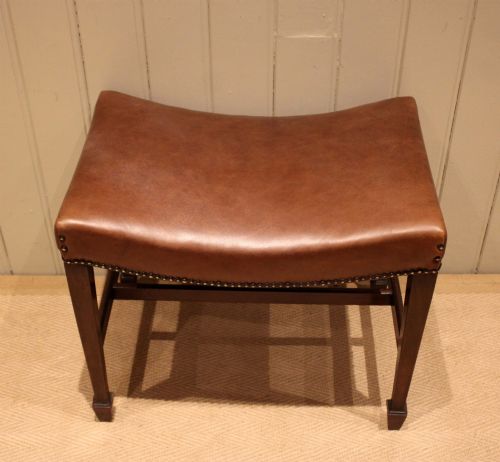 fig 1. An Edwardian mahogany stool featuring a concave tan leather seat trimmed with brass studs and supported by square tapered legs with stretchers.