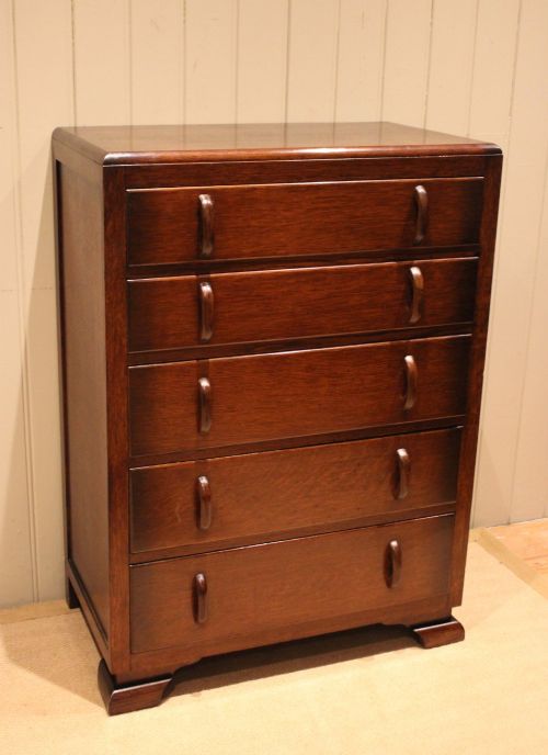 fig 1. A dark brown oak Art Deco chest of drawers featuring five stacked drawers with matching wood handles and stepped feet.