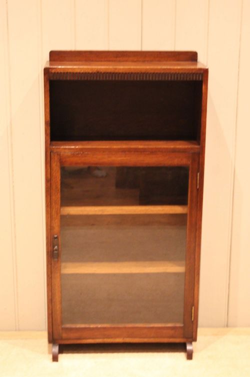 fig 1. A medium oak freestanding bookcase featuring an open top compartment above a single glass-fronted door with internal shelving.