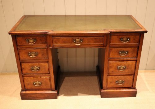 fig 1. A walnut breakfront pedestal desk featuring nine drawers with brass handles and a green leather writing insert set into the top surface.