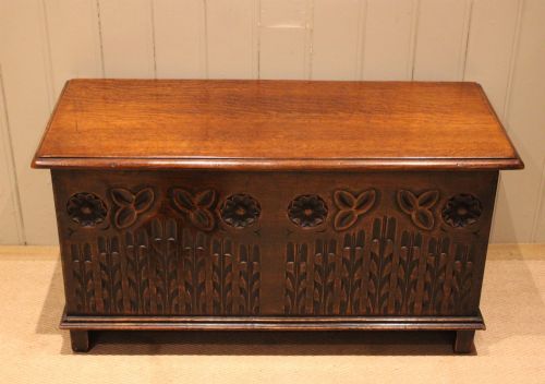 fig 1. A rectangular solid oak coffer featuring stylized floral and botanical carvings across the front panel with a smooth hinged lid.