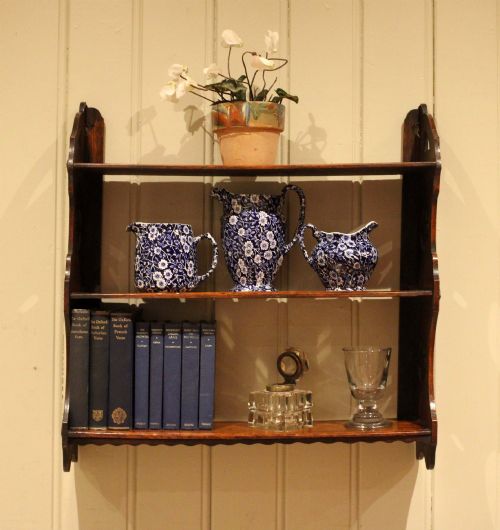 fig 1. A late nineteenth-century dark oak wall-mounted shelf unit featuring three tiers and carved geometric cutouts along the side supports.