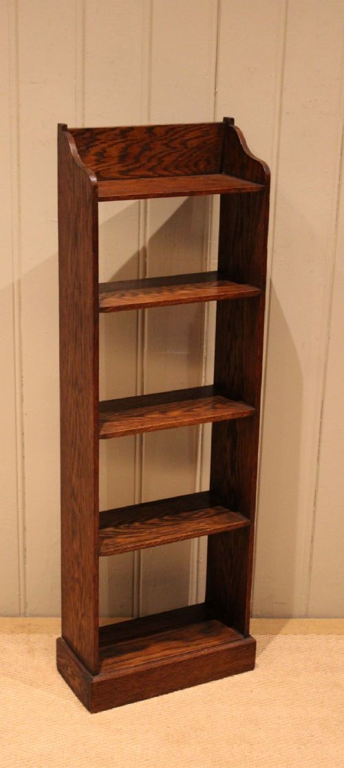 fig 1. A tall, narrow dark oak open bookcase featuring multiple shelves, a shaped gallery top, and a solid plinth base.