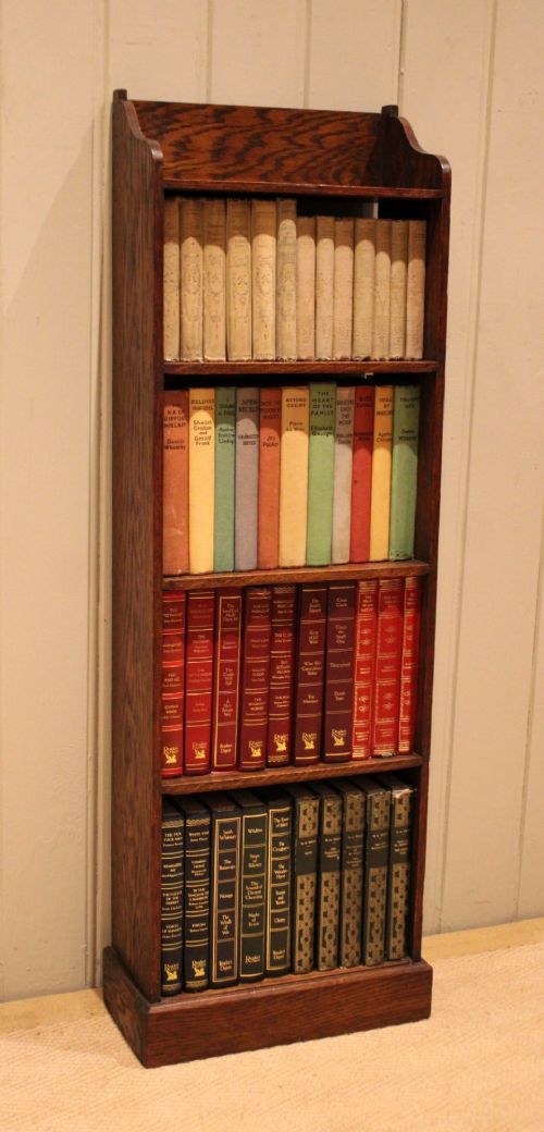 A tall, narrow dark oak open bookcase featuring multiple shelves, a shaped gallery top, and a solid plinth base. View III