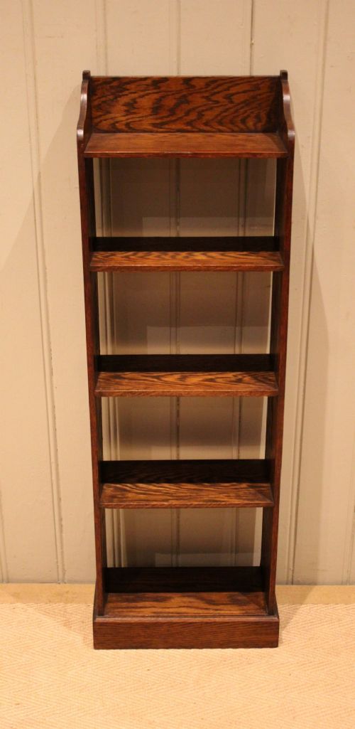 A tall, narrow dark oak open bookcase featuring multiple shelves, a shaped gallery top, and a solid plinth base. View IV