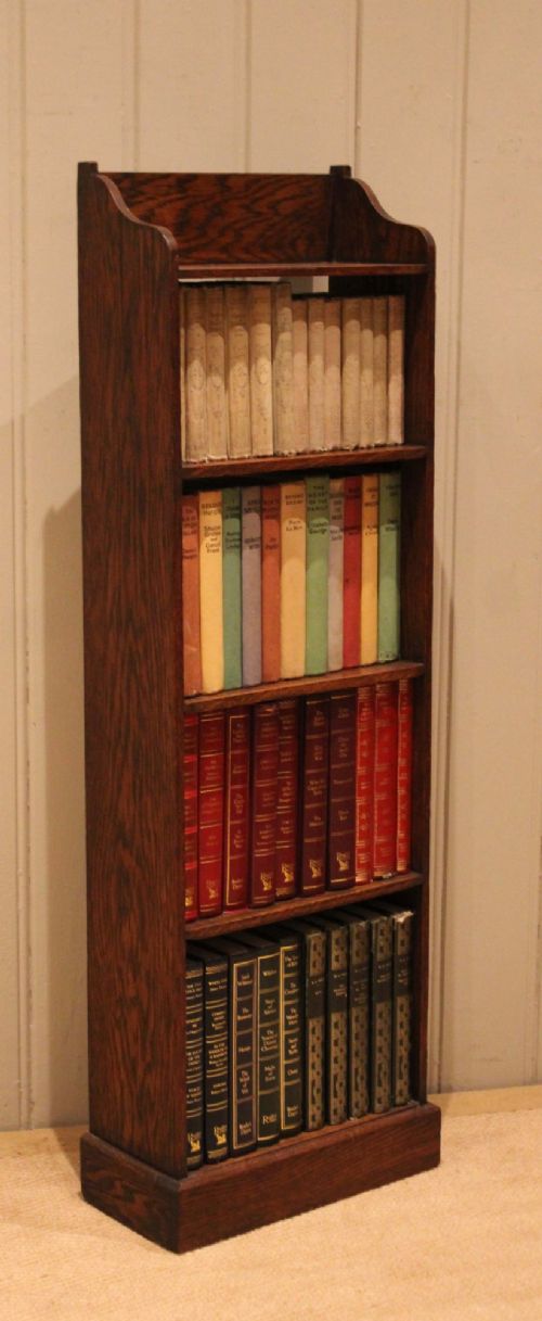 A tall, narrow dark oak open bookcase featuring multiple shelves, a shaped gallery top, and a solid plinth base. View IX