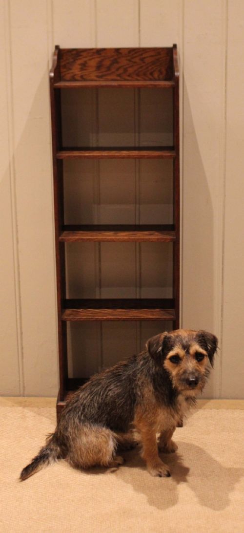 A tall, narrow dark oak open bookcase featuring multiple shelves, a shaped gallery top, and a solid plinth base. View XI