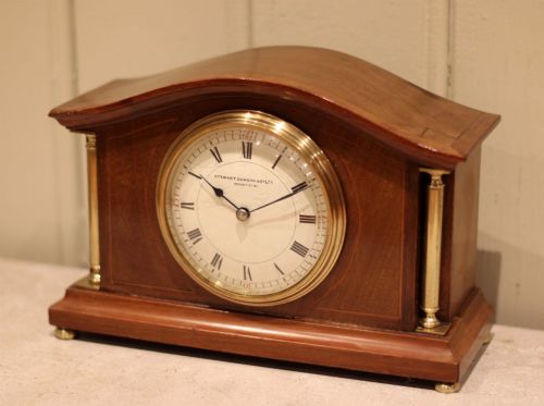fig 1. An Edwardian mahogany mantel clock featuring an arched top, brass side columns, brass feet, and a circular white dial with black Roman numerals.