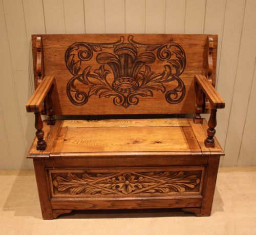 fig 1. A carved solid oak monks bench featuring a decorative back panel that tilts forward to form a table surface, turned arm supports, and a lift-up storage seat.