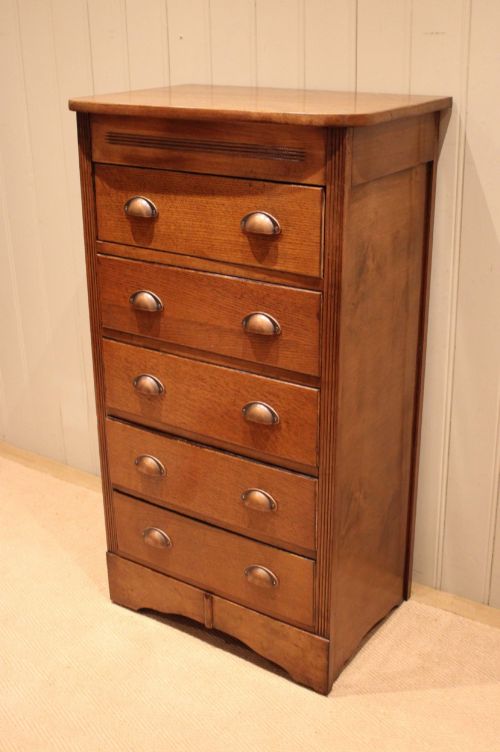 fig 1. A tall oak chest of drawers featuring five drawers with metal cup handles and reeded side detailing.